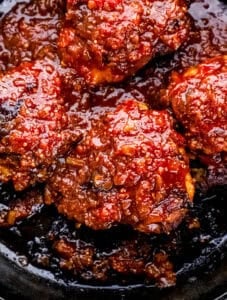 Close up view of chicken thighs topped with sauce in cast iron skillet.