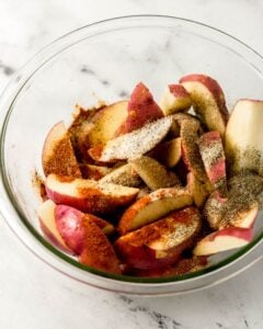 Spices added to potatoes in glass mixing bowl.