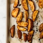 Freshly baked potato wedges on parchment lined baking sheet.