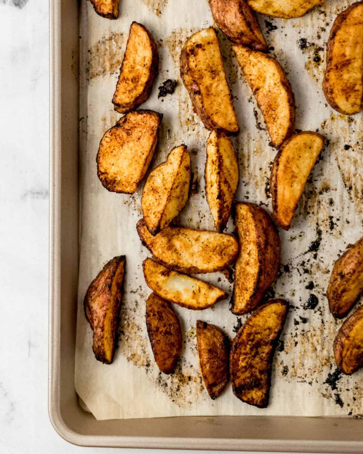Freshly baked potato wedges on parchment lined baking sheet. 