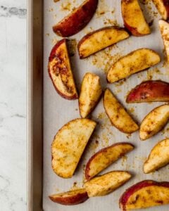 Seasoned potato wedges added to a parchment lined sheet pan.