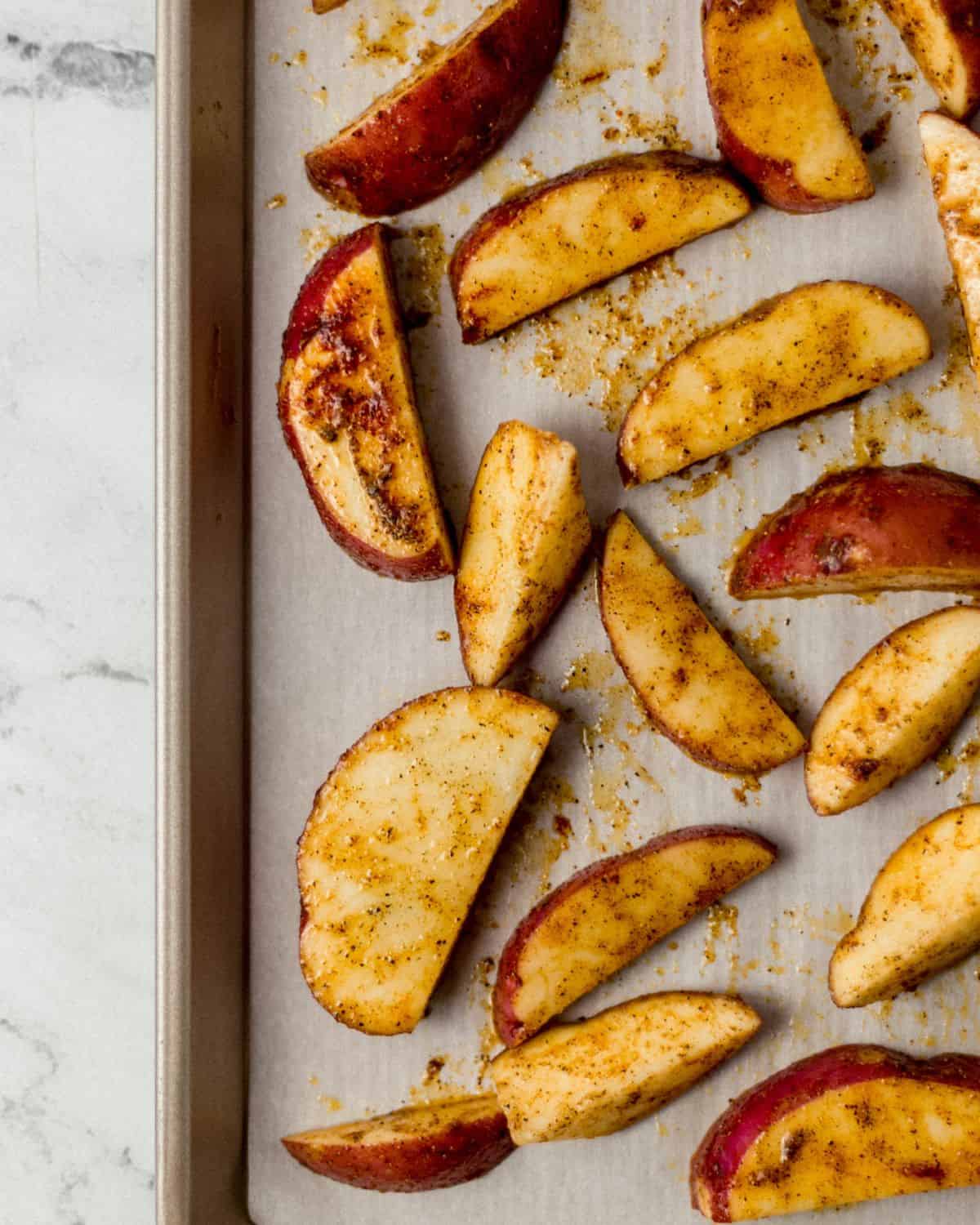 Seasoned potatoes on parchment lined baking sheet before baking in the oven. 