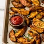 Close up front view of potatoes on parchment lined baking sheet with small bowl of ketchup.