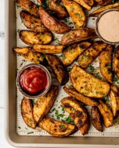 Overhead view of parchment lined baking sheet with potato wedges on it topped with fresh parsley.