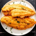 Overhead view of fried fish on white plate topped with freshly chopped parsley.