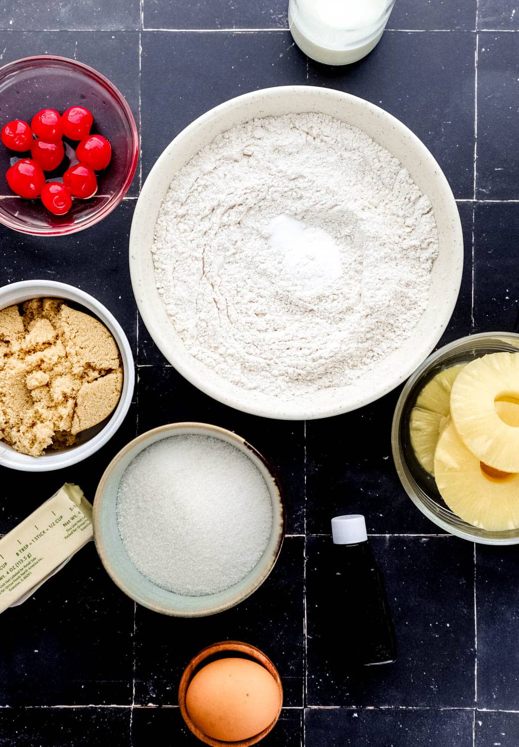 Overhead view of ingredients to make cake in separate bowls on black tile surface.