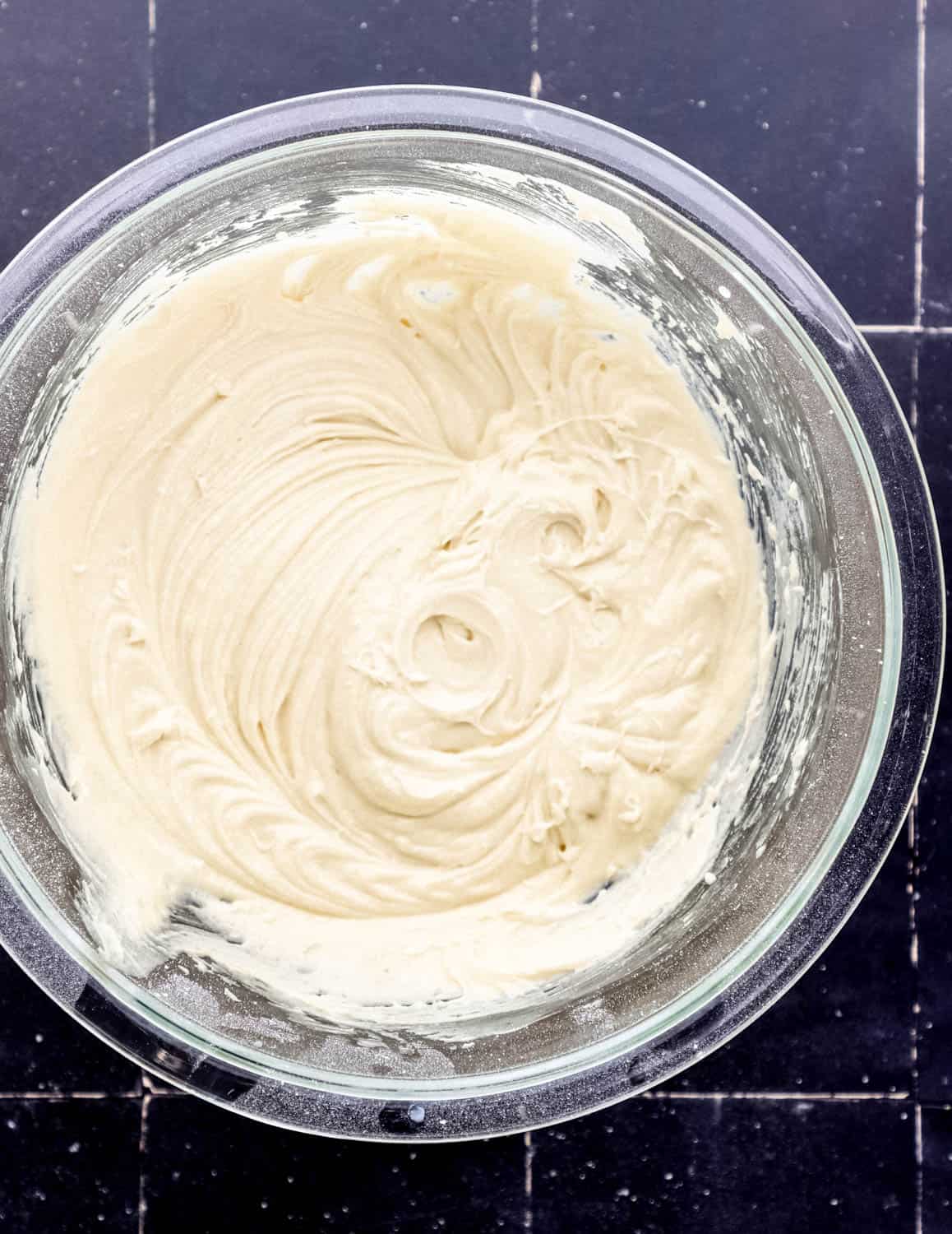 Cake mixture in large glass bowl on black tile surface. 