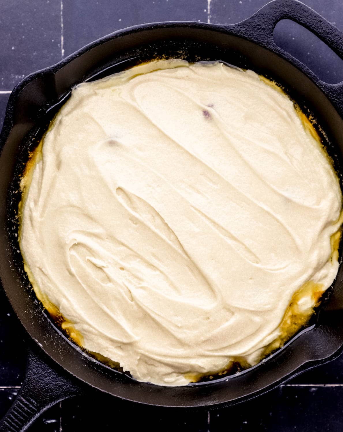 Cake mixture added to the top of the pineapple mixture in a cast iron skillet. 