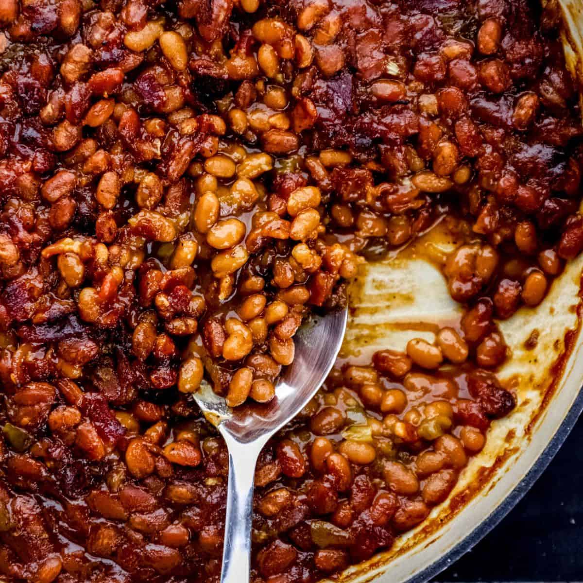 Overhead view of southern baked beans in large white braiser pan with serving spoon in it.