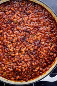 Overhead view of baked beans in braiser pan on black tile surface.
