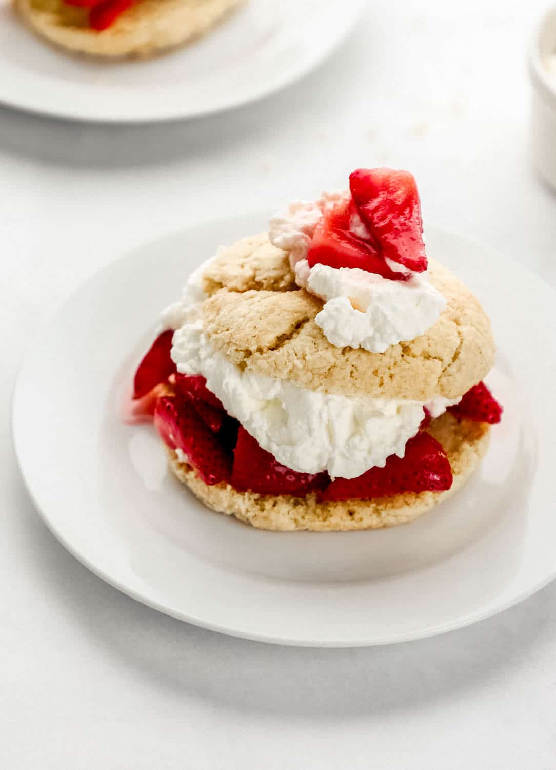 Close up side view of finished strawberry shortcake on small white plate.