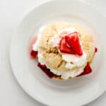 Overhead view of strawberry shortcake on white plate on top of grey surface.