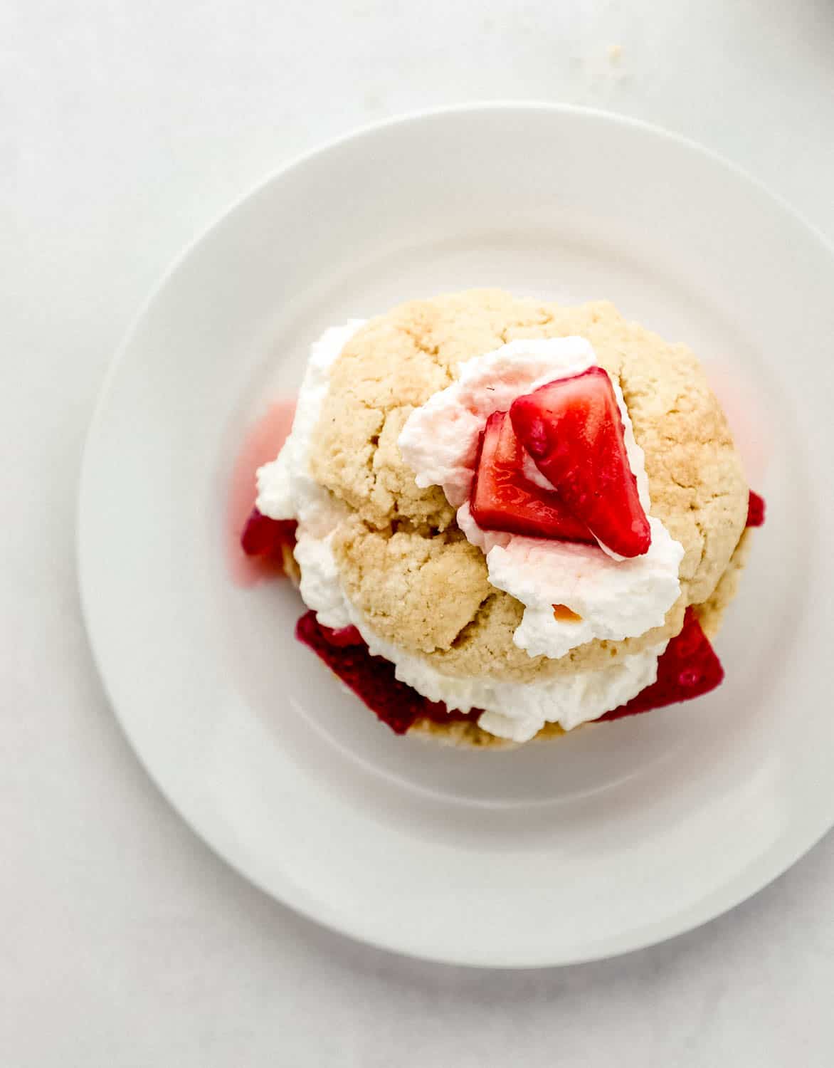 Overhead view of single assembled strawberry shortcake on white plate.