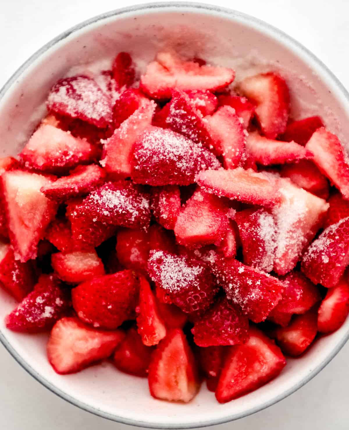Strawberries cut in half and topped with sugar in white bowl.