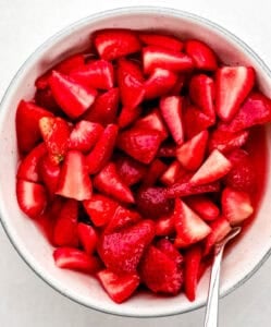 Mascerated strawberries in a white bowl with spoon.