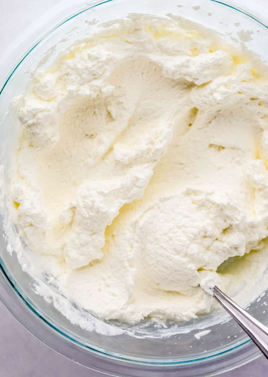 Overhead view of homemade whipped cream in large glass mixing bowl with spoon in it.