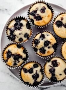Overhead view of finished muffins on white plate on top of marble surface.