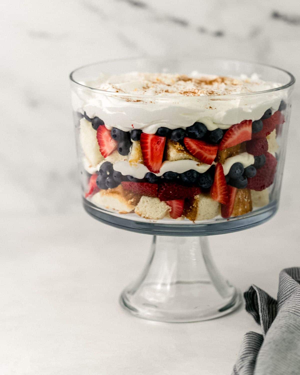 Close up side view of finished trifle by a striped cloth napkin on grey surface.