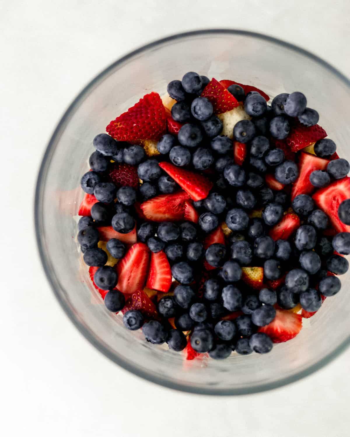 Overhead view of pound cake and berries added to glass trifle dish. 