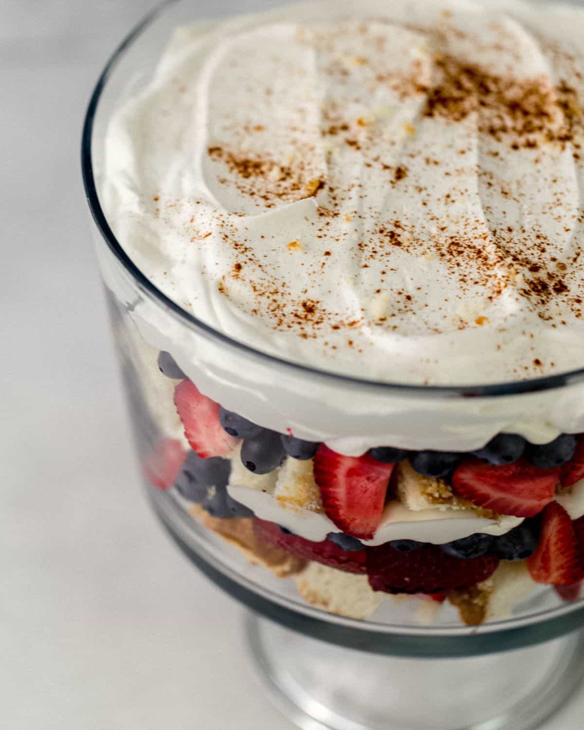 Close up side view of trifle topped with whipped topping and sprinkle of cinnamon. 