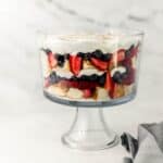 Close up side view of pound cake trifle in glass dish by cloth napkin.