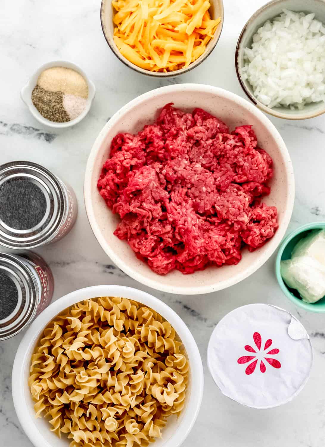 Overhead view of ingredients needed to make casserole in separate bowls and containers on marble surface. 