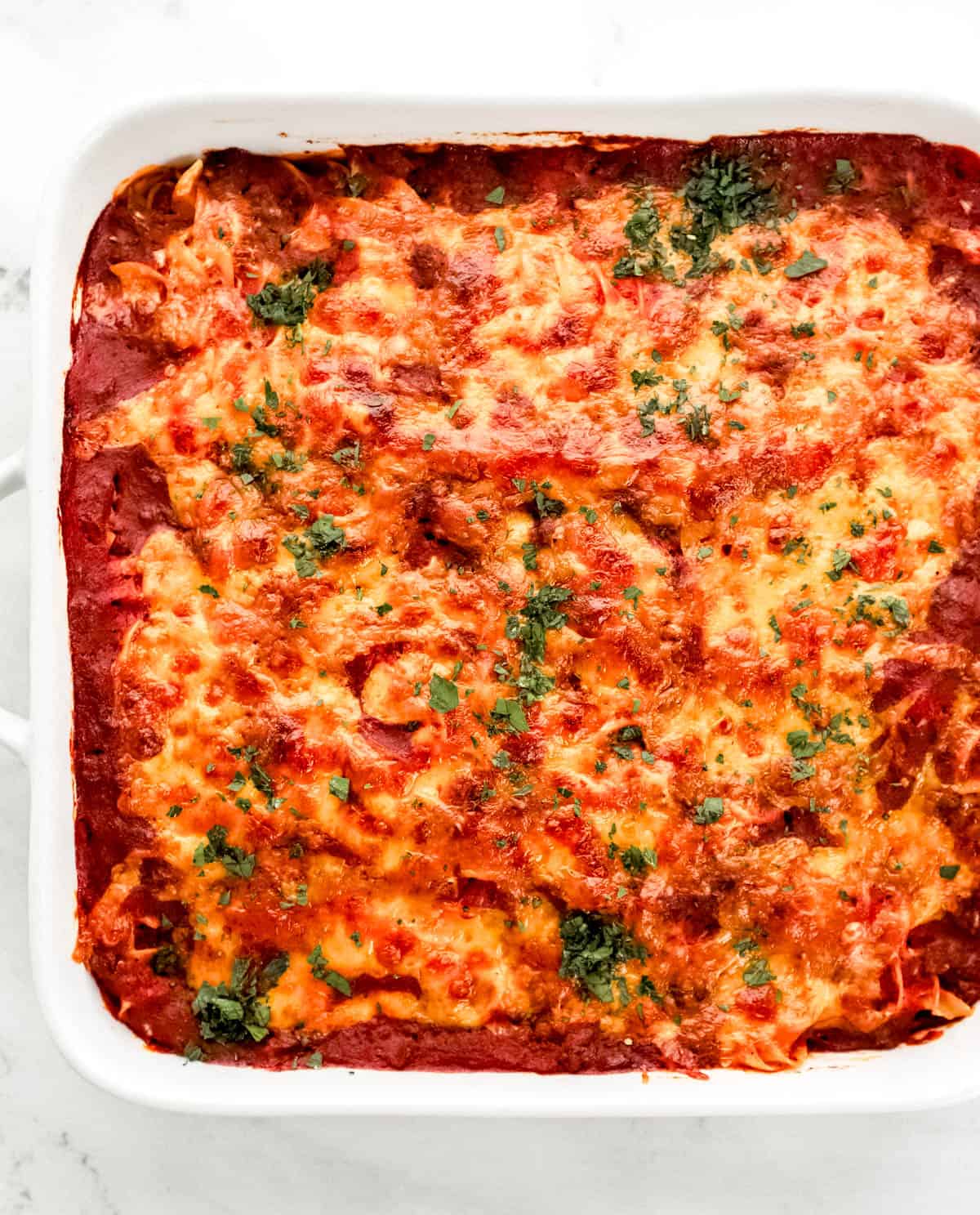 Overhead view of baked casserole in square white baking dish topped with chopped parsley. 