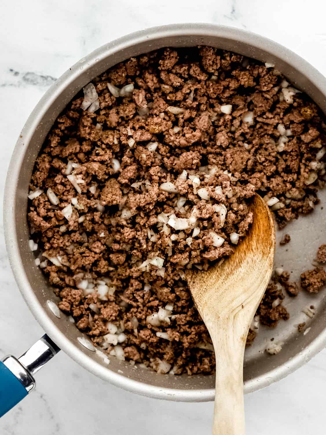 Overhead view of ground beer and onion in skillet with wooden spoon. 
