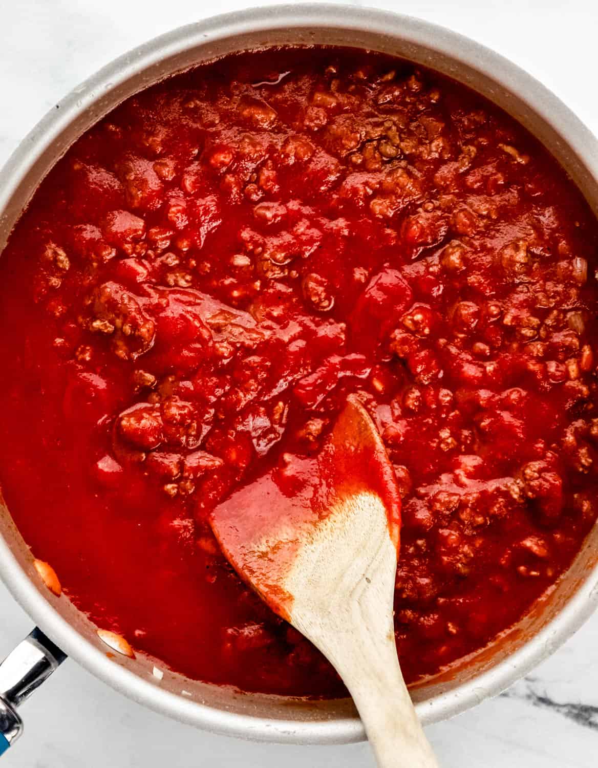 Overhead view of meat sauce in skillet with wooden spoon. 