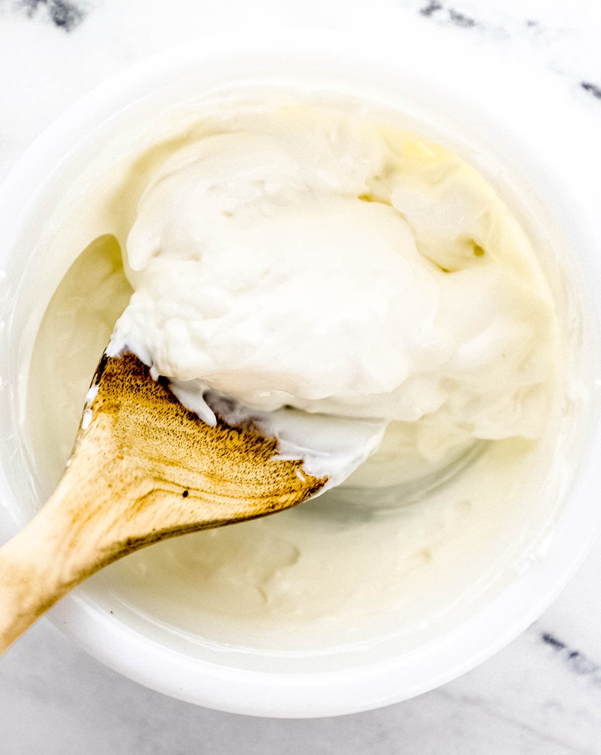 Cream cheese and sour cream in white mixing bowl with wooden spoon. 