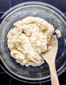 Overhead view of hush puppy batter in glass mixing bowl with wooden spoon.