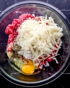 Ingredients to make meatballs added to large glass mixing bowl.