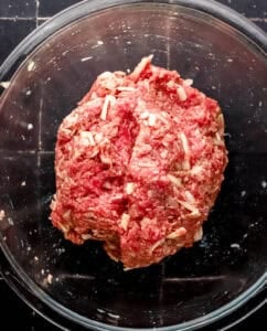 Meatball ingredients combined in large glass mixing bowl.
