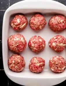 Overhead view of prepared meatballs in white square baking dish.