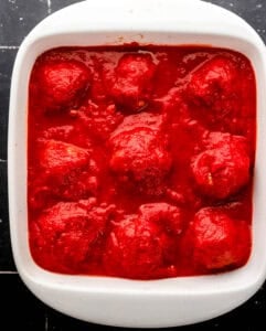 Meatballs topped with sauce in white baking dish.