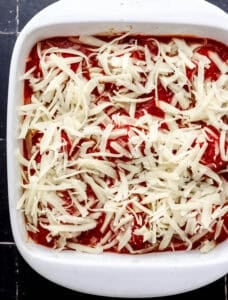 Meatballs in baking dish topped with shredded cheese before baking.