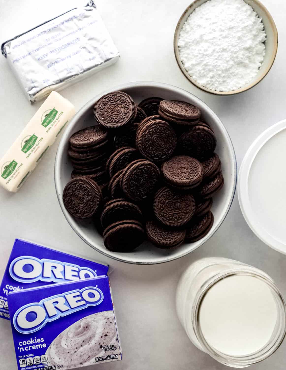 Ingredients needed to make oreo delight in separate bowls and containers on grey surface. 
