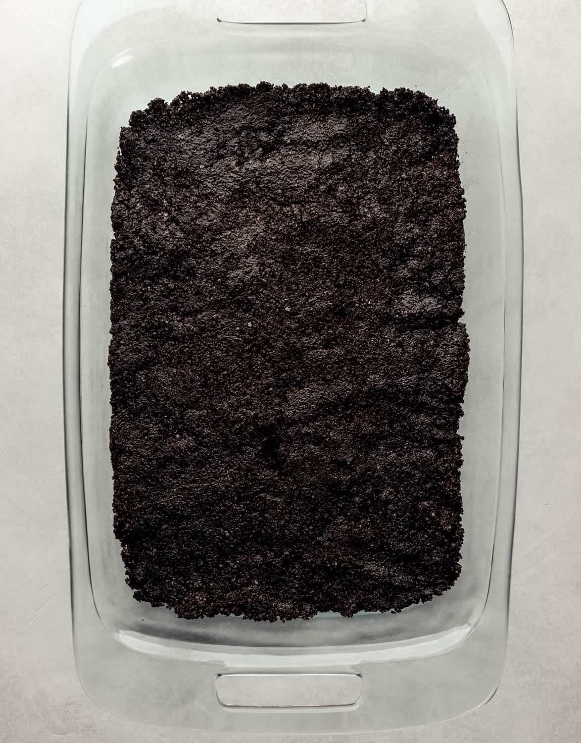Overhead view of cookie crust in rectangle glass baking dish on grey surface. 