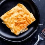 Overhead view of serving of finished casserole on small black plate by a fork.