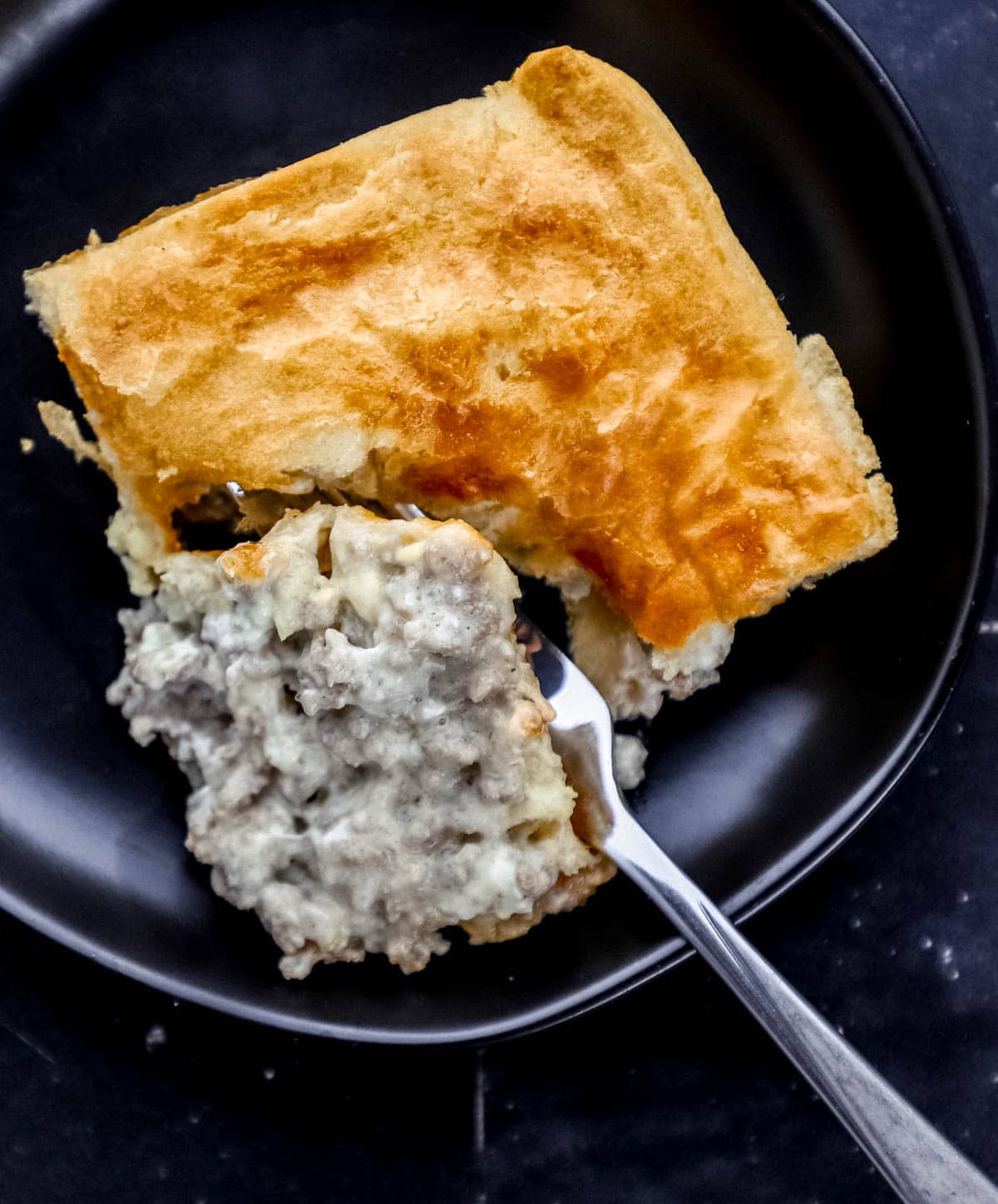 Overhead view of single serving of casserole on black plate with a fork cutting into it.