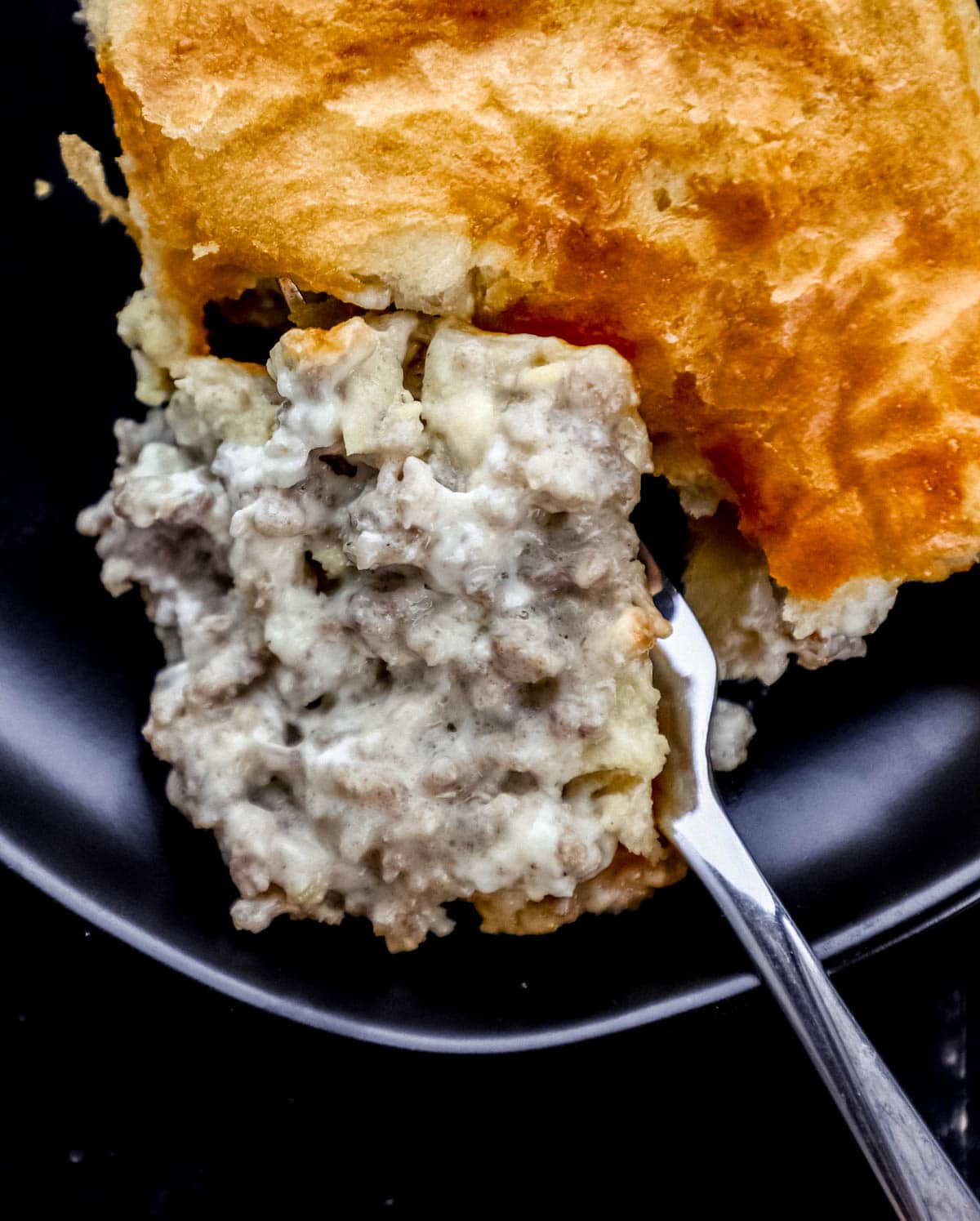 Close up overhead view of serving of casserole on black plate with a fork cutting into it. 