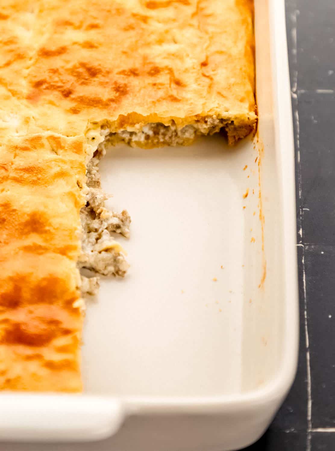 Close up front view of casserole in white baking dish with some removed. 