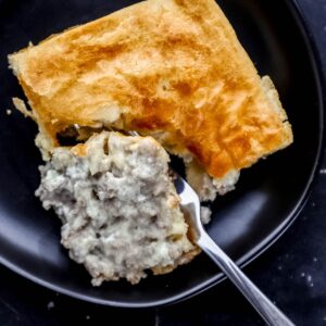 Overhead view of single serving of casserole on black plate with fork cutting into it.