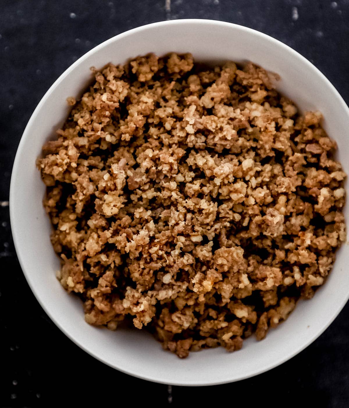 Overhead view of cooked ground sausage in a white bowl. 