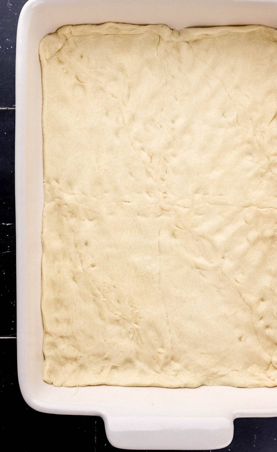 Crescent roll dough added to the bottom of a white rectangle baking dish. 