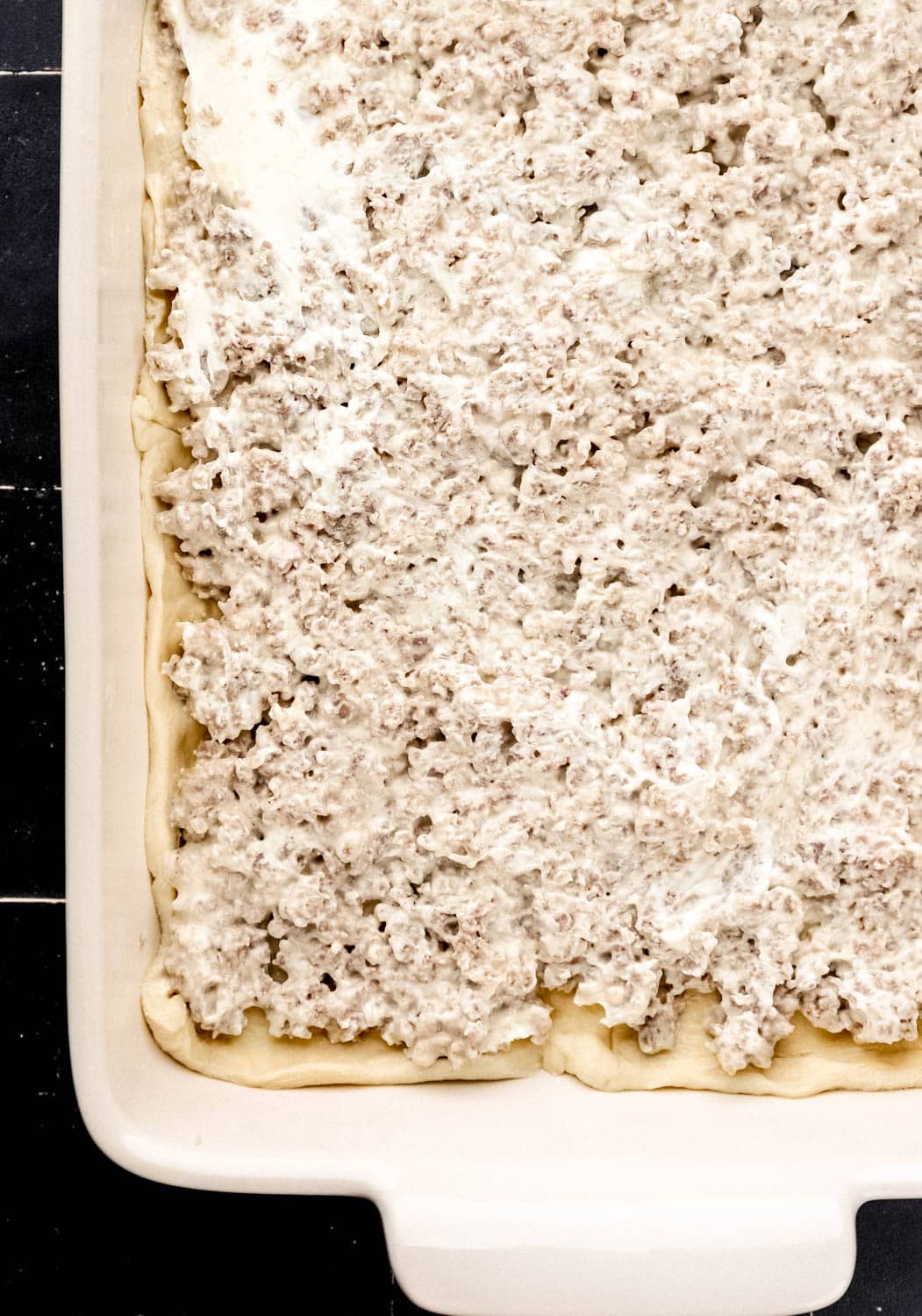 Overhead view of sausage and cream cheese mixture added to crescent dough in a white baking dish. 