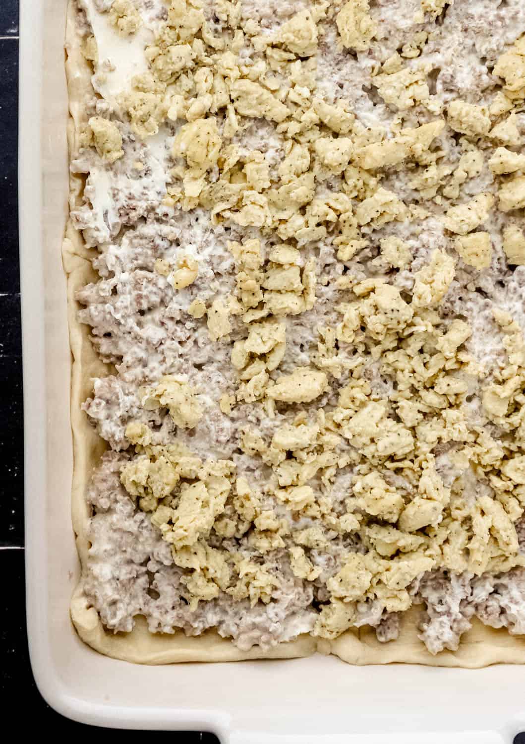 Scrambled eggs added on top of the sausage mixture and dough in a baking dish. 