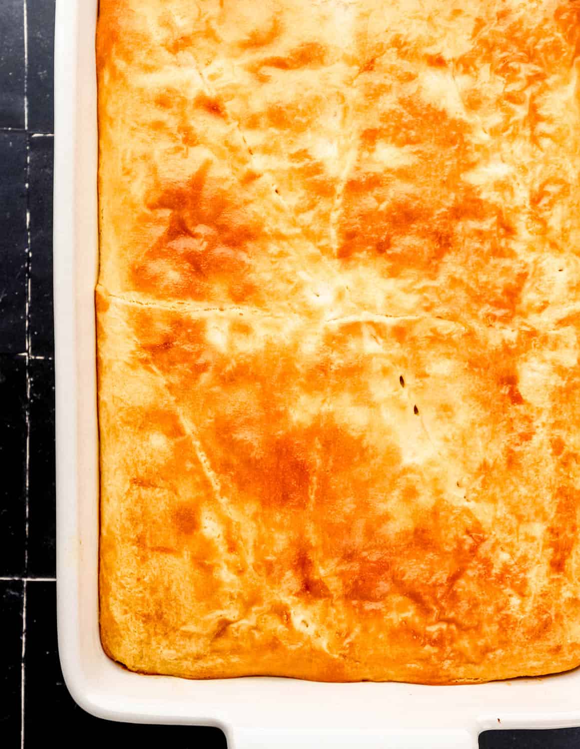 Overhead view of baked casserole in white baking dish on black tile surface. 