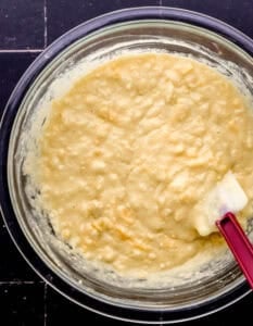 Cornbread mixture in glass mixing bowl with spatula.
