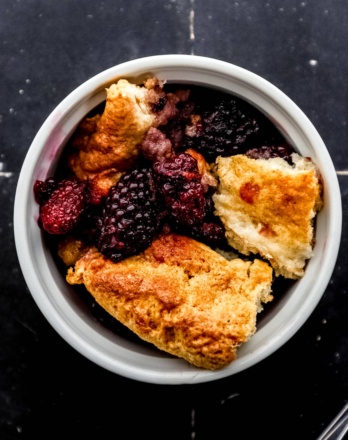 Overhead view of single serving of cobbler in small white bowl by a spoon. 